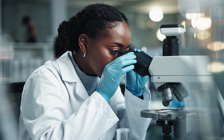 Scientifique portant des gants regardant au microscope dans un laboratoire.