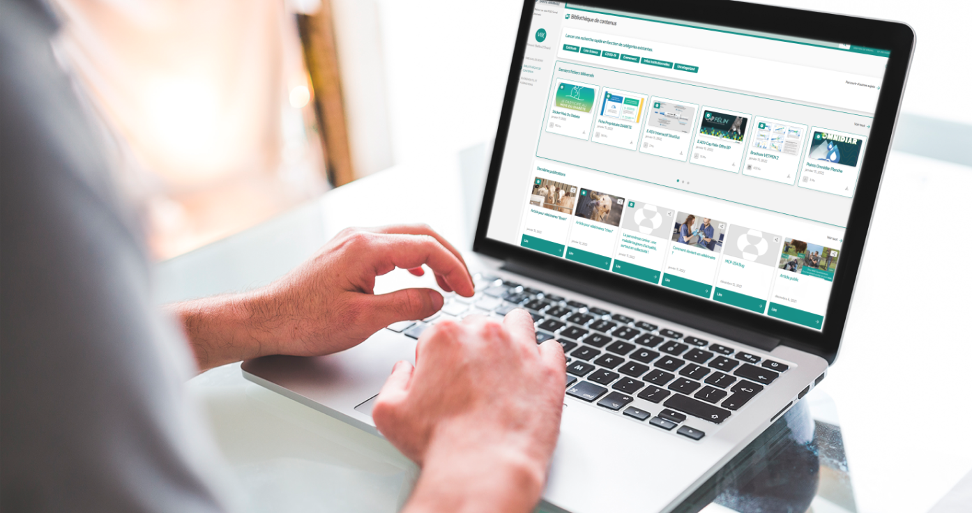 Vue rapprochée des mains d'une personne utilisant un ordinateur portable affichant une bibliothèque de contenus numériques pour vétérinaires.